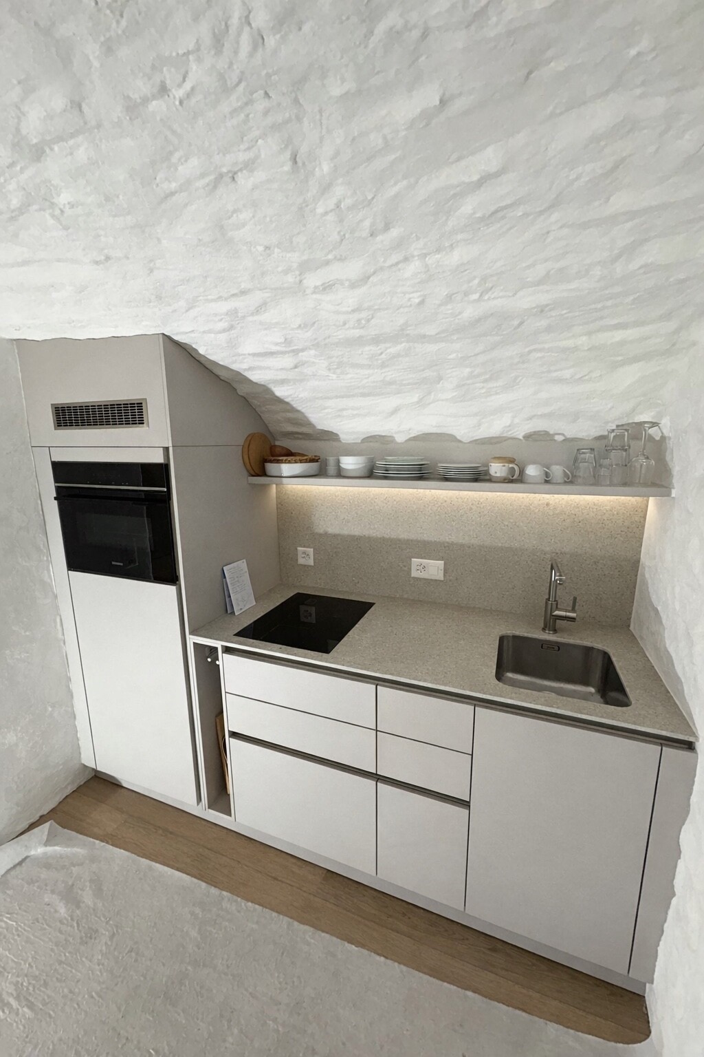 Moderne minimalistische Küche mit weißem Interieur, Arbeitsplatte, Herd, Spüle und Hängeregal in einem hellen Raum.