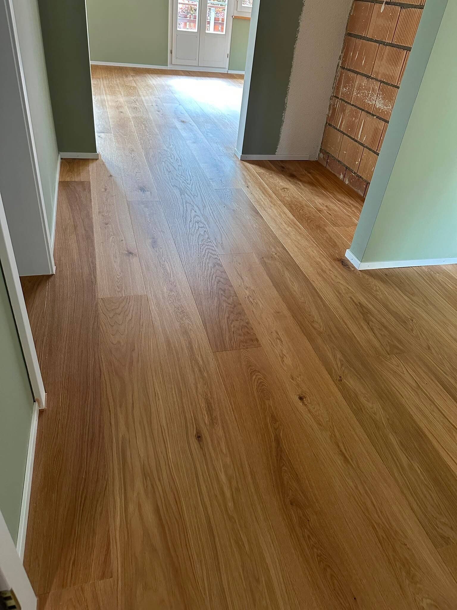 Renoviertes Zimmer mit neuem Laminatboden und grünen Wänden, im Tageslicht strahlend.