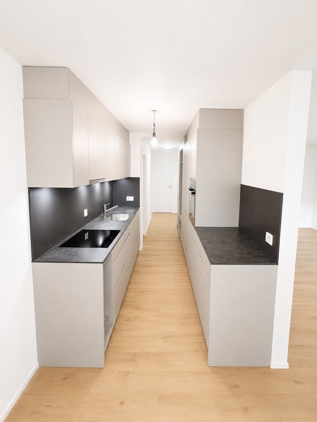 Moderne Einbauküche in Grautönen mit Holzfußboden und eleganter Beleuchtung, stilvolles Design für zeitgemäße Wohnräume.