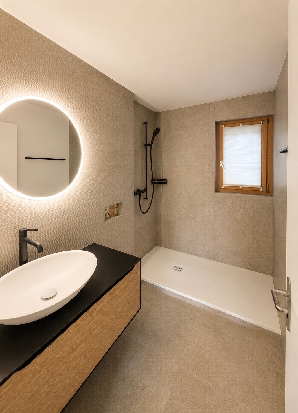 Modernes Badezimmer mit beleuchtetem Rundspiegel, Waschbecken, schwarzer Armatur und begehbarer Dusche.