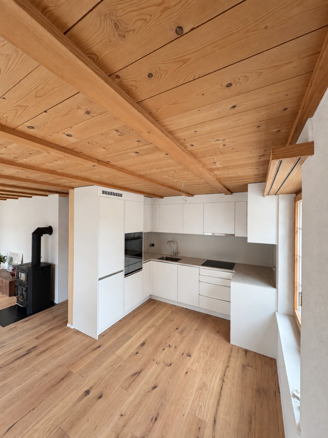 047250ef-4fb8-4927-af73-e8790a478b8a Moderne Küche mit Holzbalkendecke und Parkettboden, ausgestattet mit weißen Schränken und minimalistischem Design.