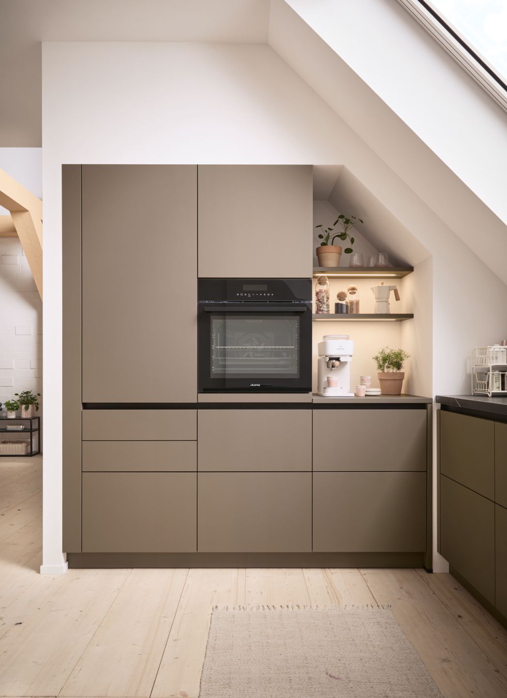 047250ef-4fb8-4927-af73-e8790a478b8a Moderne Küche mit eingebauten Schränken, Backofen und kleiner Kaffeestation unter Dachschräge.